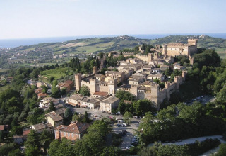Luftfoto af en middelalderlig befæstet by nær Pesaro i Marche, Italien, omgivet af frodige bakker og hav.
