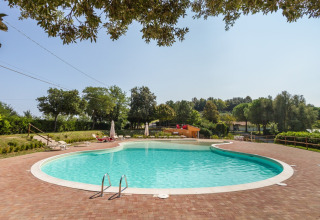 Piscina all’aperto al Camping Paradiso nelle Marche, Italia, circondata dal verde e lettini prendisole.