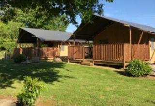 Two cozy safari tents with wooden decks at Camping de Kerleyou holiday park in Brittany, France, surrounded by greenery.