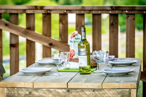 Mesa exterior puesta con vino y copas en Camping de Kerleyou, parque vacacional en Bretaña, Francia.