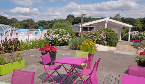 Zona exterior con mesas coloridas, flores y piscina en Camping de Kerleyou, parque de vacaciones en Bretaña, Francia.