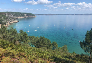 Vista su acque blu, barche a vela e vegetazione dal Camping de Kerleyou in Bretagna, Francia.