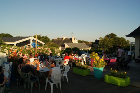 People dining outdoors at sunset at Camping de Kerleyou holiday park in Brittany, France, surrounded by flowers.