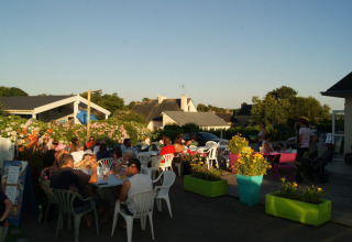People dining outdoors at sunset at Camping de Kerleyou holiday park in Brittany, France, surrounded by flowers.