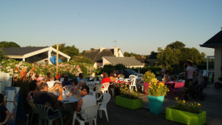 People dining outdoors at sunset at Camping de Kerleyou holiday park in Brittany, France, surrounded by flowers.