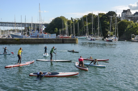 Folk nyder stand up paddleboarding på vandet nær lystbåde og både ved Camping de Kerleyou i Bretagne.