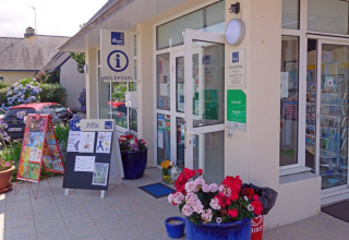 Receptionen ved Camping de Kerleyou i Bretagne, Frankrig, med blomster, informationsskilte og parkerede biler.