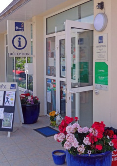 Reception of Camping de Kerleyou in Brittany, France, featuring flowers, information boards, and parked cars.