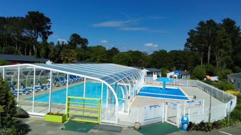 Zona de piscina al aire libre con piscina cubierta y tumbonas en Camping de Kerleyou, Bretaña, Francia.