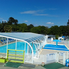 Outdoor pool area with covered swimming pool and loungers at Camping de Kerleyou, Brittany, France.
