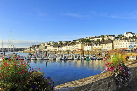Vista del puerto de Douarnenez en Bretaña, Francia, con barcos coloridos, flores y edificios históricos al sol.