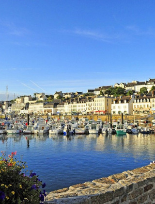 View of Douarnenez harbor in Brittany, France, with colorful boats, flowers, and sunlit historic buildings.