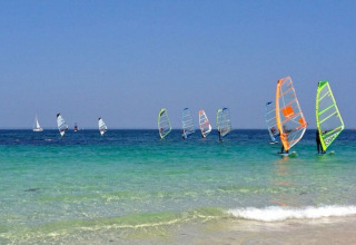 Windsurfers and sailboats on the clear blue water at Camping de Kerleyou holiday park in Brittany, France.