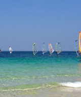 Windsurfers and sailboats on the clear blue water at Camping de Kerleyou holiday park in Brittany, France.