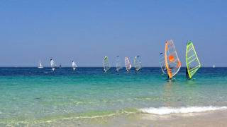 Windsurfers and sailboats on the clear blue water at Camping de Kerleyou holiday park in Brittany, France.