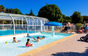 Børn leger i swimmingpool ved Camping de Kerleyou, solrig dag, feriested i Bretagne, Frankrig.