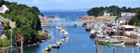 View of Douarnenez harbor in Brittany, France, showing sailboats, lush greenery, and the open sea.