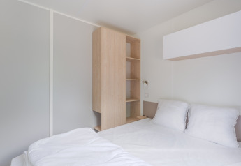 Moderne, minimalistisk hytteindretning på Camping Seasonova du Chêne i Frankrig, med en seng og trægarderobe.