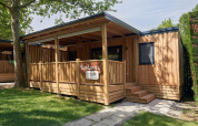 Cabaña de madera SunLodge Katsura en Camping Gasparina, Italia, con terraza y rodeada de vegetación.