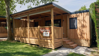The SunLodge Katsura wooden cabin at Camping Gasparina in Italy with porch, trees, and green lawn.