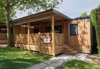 The SunLodge Katsura wooden cabin at Camping Gasparina in Italy with porch, trees, and green lawn.