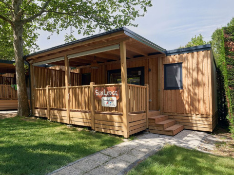 Cabaña de madera SunLodge Katsura en Camping Gasparina, Italia, con terraza y rodeada de vegetación.