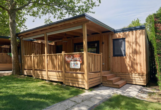 Cabaña de madera SunLodge Katsura en Camping Gasparina, Italia, con terraza y rodeada de vegetación.