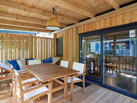 Terraza de madera cubierta en SunLodge Katsura, Camping Gasparina, Italia, con mesa de comedor y sillas cómodas.