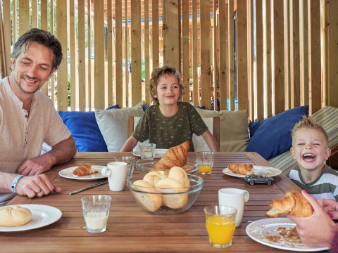 Familia desayunando con croissants y jugo en la terraza de SunLodge Katsura en Camping Gasparina, Italia.