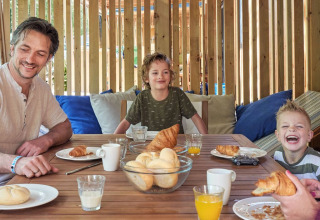 Famille prenant le petit-déjeuner avec croissants et jus sur la terrasse de SunLodge Katsura à Camping Gasparina, Italie.