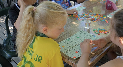 Kinderen spelen bingo met gekleurde fichekes aan een tafel op Camping Saint Amand in Auvergne-Rhône-Alpes, Frankrijk.