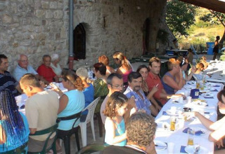 Gruppo di persone che condividono un pasto all'aperto su un lungo tavolo al Camping Saint Amand, Auvergne-Rhône-Alpes, Francia.