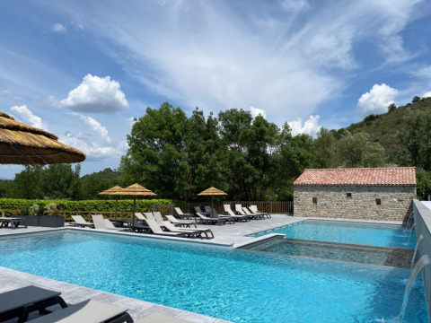 Piscina all’aperto con lettini e ombrelloni di paglia al Camping Saint Amand, Auvergne-Rhône-Alpes, Francia.