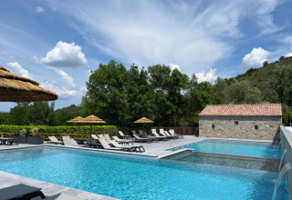 Piscina all’aperto con lettini e ombrelloni di paglia al Camping Saint Amand, Auvergne-Rhône-Alpes, Francia.