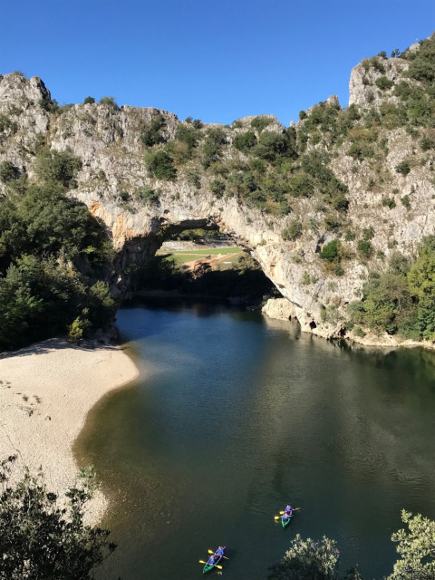 Personas en kayak por un río bajo un arco natural de piedra en Camping Saint Amand, Auvergne-Rhône-Alpes, Francia.