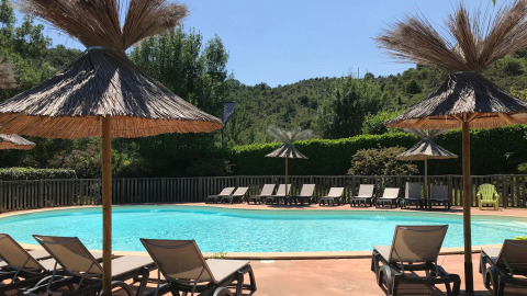 Outdoor swimming pool area with sun loungers and thatched umbrellas at Camping Saint Amand, France.