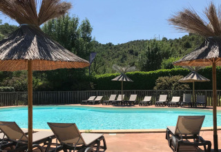 Außenpool mit Sonnenliegen und Strohdächern im Camping Saint Amand in Auvergne-Rhône-Alpes, Frankreich.