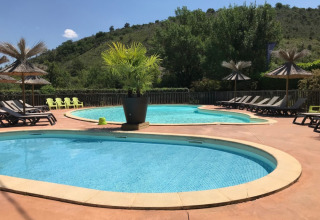 Udendørs swimmingpool med liggestole og parasoller på Camping Saint Amand i Auvergne-Rhône-Alpes, Frankrig.