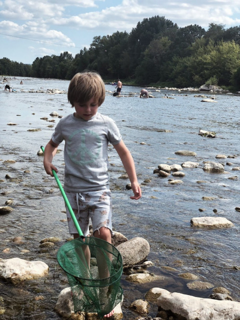 Niño jugando con red de pesca en el río en Camping Saint Amand, Auvergne-Rhône-Alpes, Francia, día de verano.