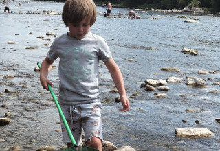 Bambino che gioca con il retino nel fiume al Camping Saint Amand, Auvergne-Rhône-Alpes, Francia, giornata estiva.