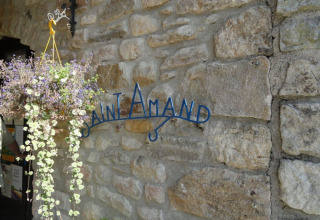 Indgang til Camping Saint Amand med en hængende plantekurv og stenvæg, Auvergne-Rhône-Alpes, Frankrig.
