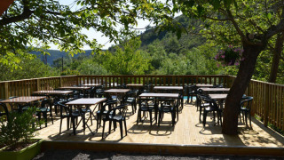Terrazza all'aperto con tavoli e sedie sotto gli alberi al Camping Saint Amand in Auvergne-Rhône-Alpes, Francia.