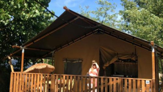 Tenda safari con servizi igienici al Camping Saint Amand in Francia, persona sulla veranda soleggiata.