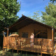 Safari-telt med sanitære faciliteter på Camping Saint Amand i Frankrig med person på verandaen under solskin.