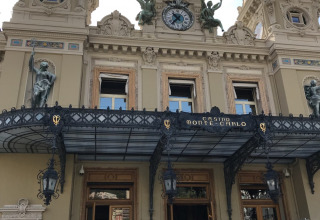 Facade af det ikoniske Casino de Monte-Carlo med dekorative statuer og ur, set fra trappen foran indgangen.