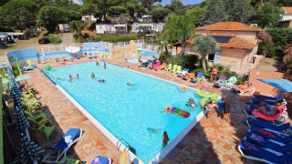 Udendørs swimmingpool med feriegæster på liggestole og børn der leger ved Camping Les Lauriers Roses i Frankrig.