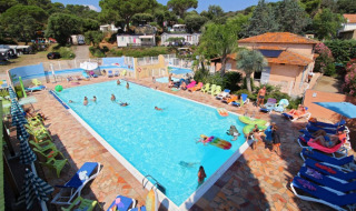 Udendørs swimmingpool med feriegæster på liggestole og børn der leger ved Camping Les Lauriers Roses i Frankrig.