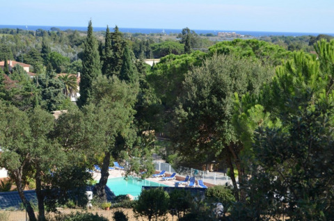 View of Camping Les Lauriers Roses with swimming pool, lush trees, and distant sea in Provence-Alpes-Côte d’Azur, France.