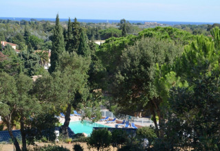 Vista del Camping Les Lauriers Roses con piscina, alberi rigogliosi e mare distante in Provenza-Alpi-Costa Azzurra, Francia.