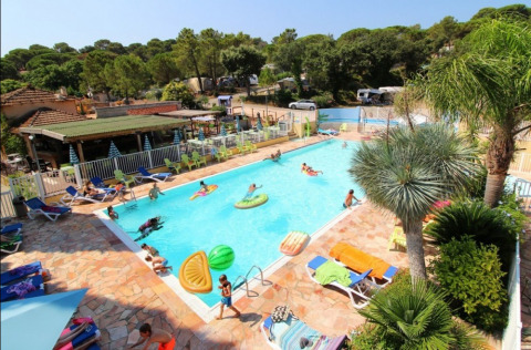Piscina exterior concurrida en Camping Les Lauriers Roses, en Provence-Alpes-Côte d’Azur, Francia, rodeada de vegetación.